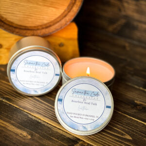 Leather 6oz candle tin with bourbon barrel in the background.