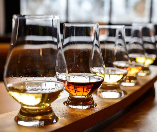 Image of a flight of bourbon vs scotch in glencairn glasses placed on a wooden flight board 