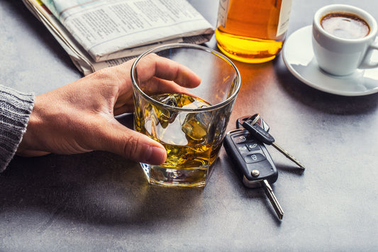 Photo of a man's hand holding a rocks glass of whiskey next to a set of car keys