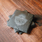 Stack of 4 black slate drink coasters with the Bourbon Real Talk logo etched on them.