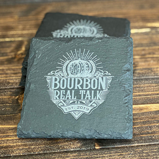 Stack of 4 black slate drink coasters with the Bourbon Real Talk logo etched on them.