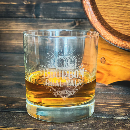 Rocks glass with the Bourbon Real Talk logo etched on the front, whiskey is in the glass
