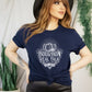 woman with red hair, black hat, black leather pants and a navy Bourbon Real Talk shirt, tied in the front