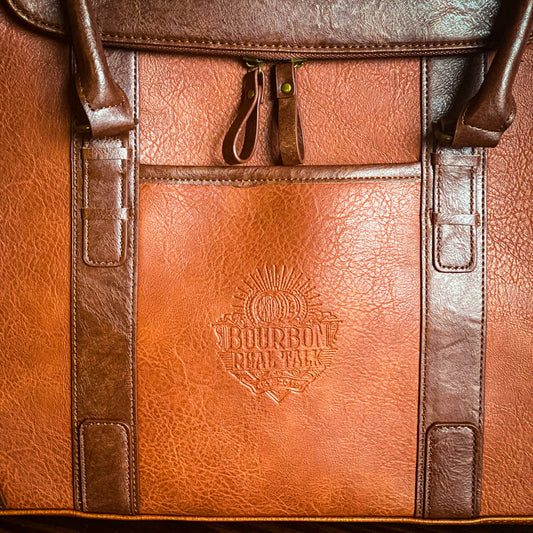 Front of the 6 Bottle Whiskey Carrier, with front pocket, zipper around the top, shoulder strap and handles, shows embossed Bourbon Real Talk logo on the front pocket