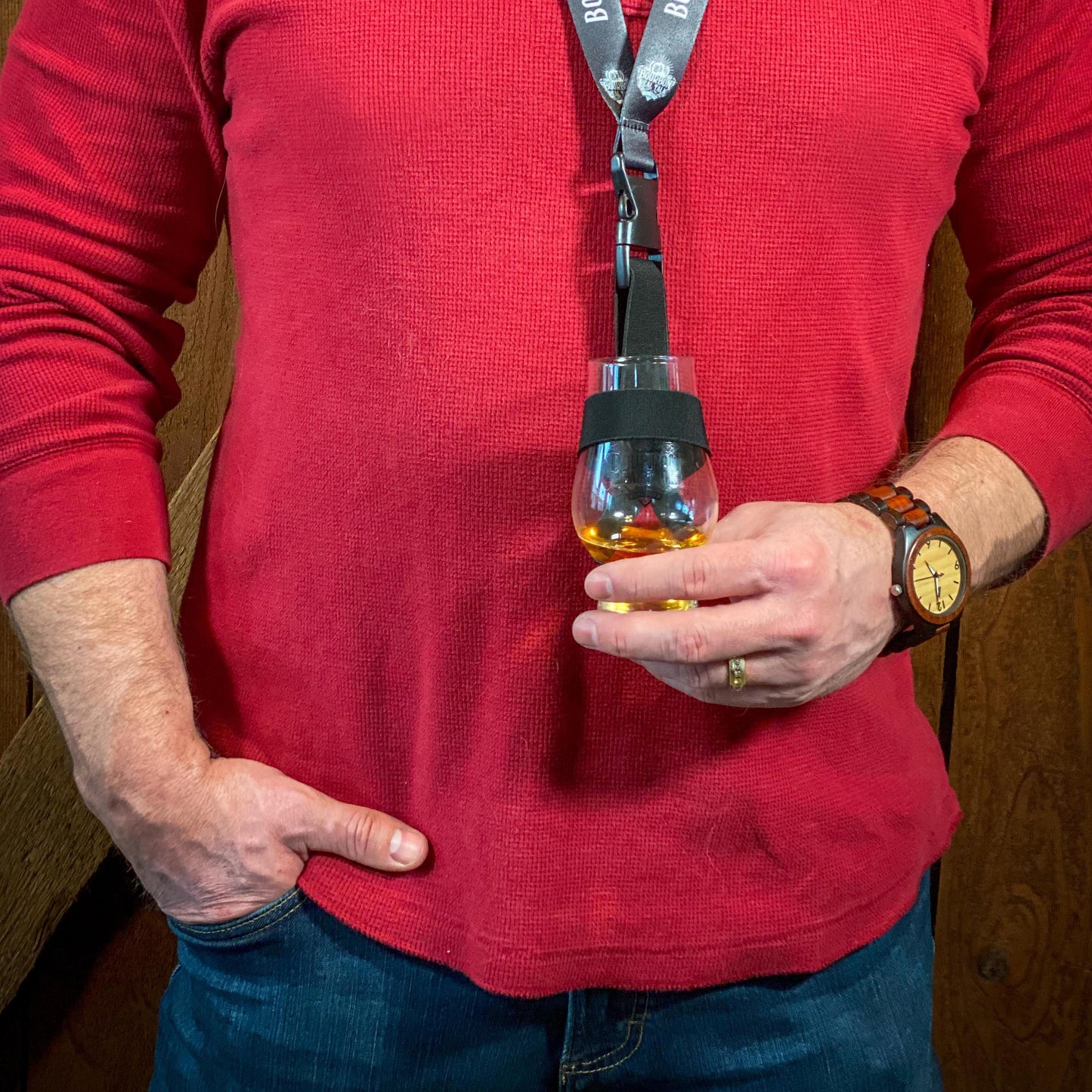 Man in a red shirt wearing The Bourbon Real Talk Laynard, holding a tasting glass filled with whiskey 