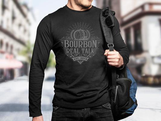Man wearing a long sleeved Bourbon Real Talk shirt with a silver logo, holding a backpack.